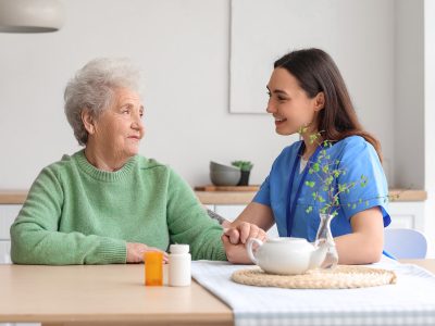 Young caregiver with senior woman holding hands in kitchen